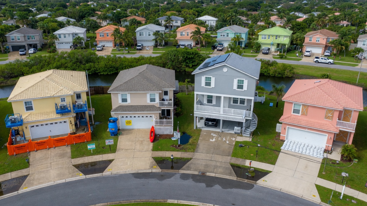 Ultra-realistic 8K aerial view of Lee County Florida residential neighborhood highlighting different flood proofing approaches on neighboring homes, clear daylight, educational perspective